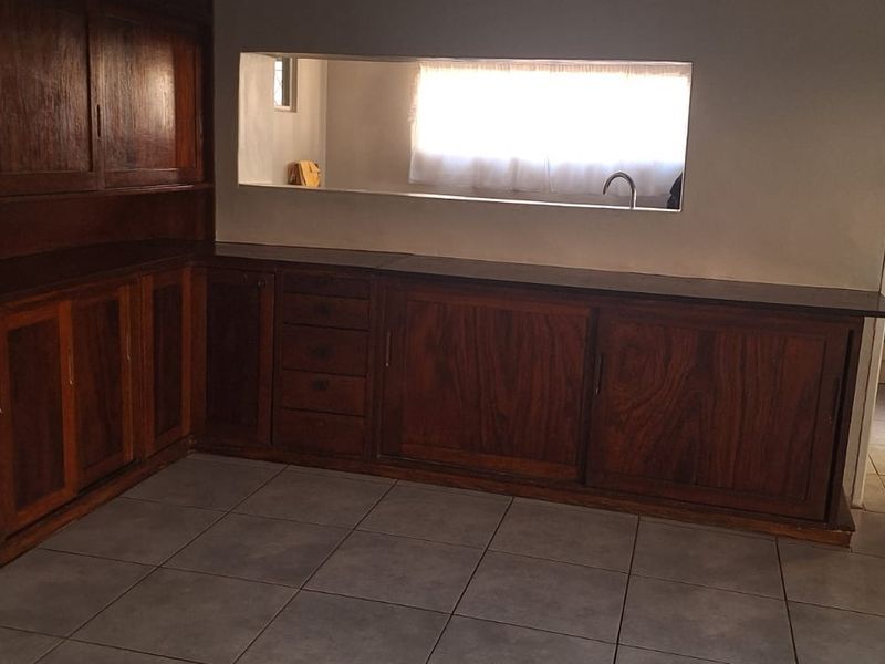 A functional kitchen area featuring extensive built-in wooden cabinetry, tiled flooring, and a convenient pass-through window connecting to the adjacent space.