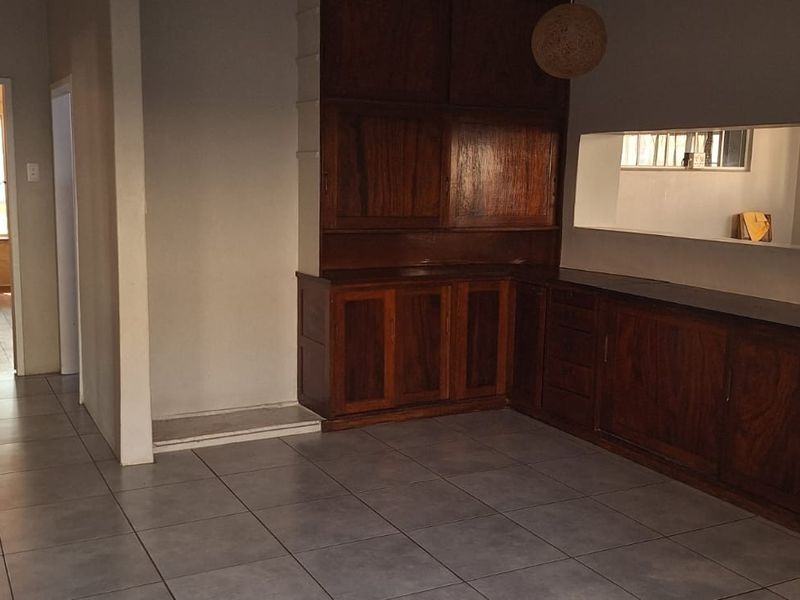 Spacious living area featuring built-in wooden cabinetry, neutral tiled flooring, and a wall-mounted mirror, offering a versatile layout for interior design.
