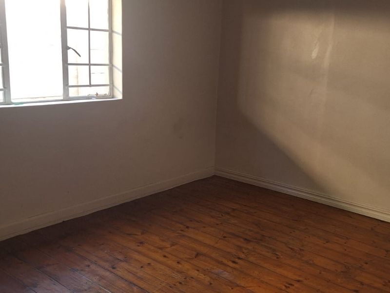 An empty bedroom featuring original timber flooring and a window fitted with security bars, offering a blank canvas for interior design.