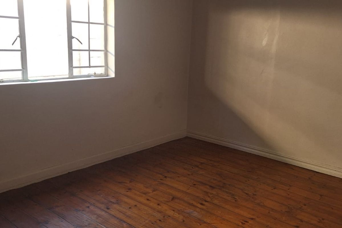 An empty bedroom featuring original timber flooring and a window fitted with security bars, offering a blank canvas for interior design.