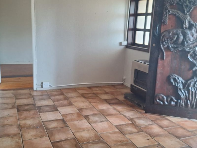 An empty living area featuring terracotta floor tiles, a built-in wood-burning fireplace, and a decorative carved wooden door leading to the exterior.