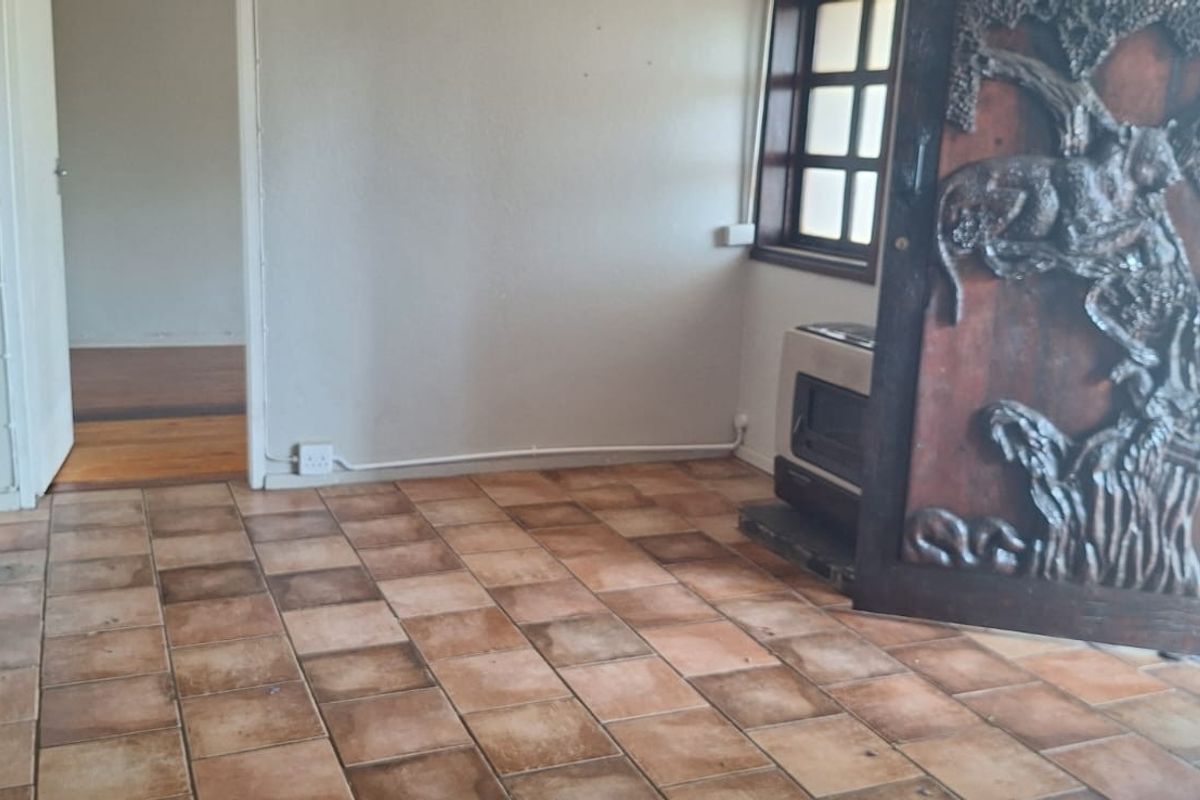 An empty living area featuring terracotta floor tiles, a built-in wood-burning fireplace, and a decorative carved wooden door leading to the exterior.