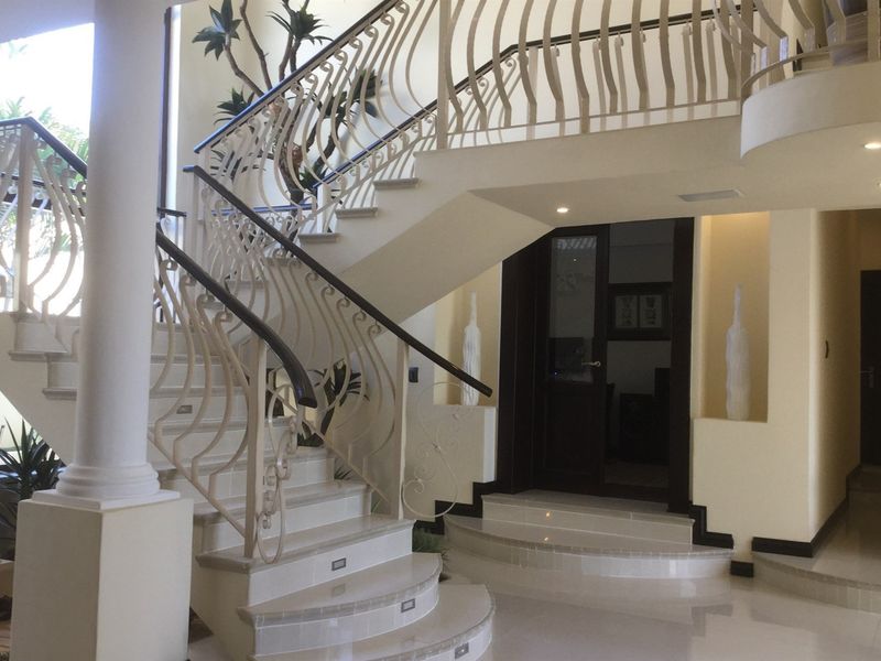 Grand entrance hall featuring a sweeping stone staircase with decorative wrought iron railings, recessed lighting, and polished tiled flooring.