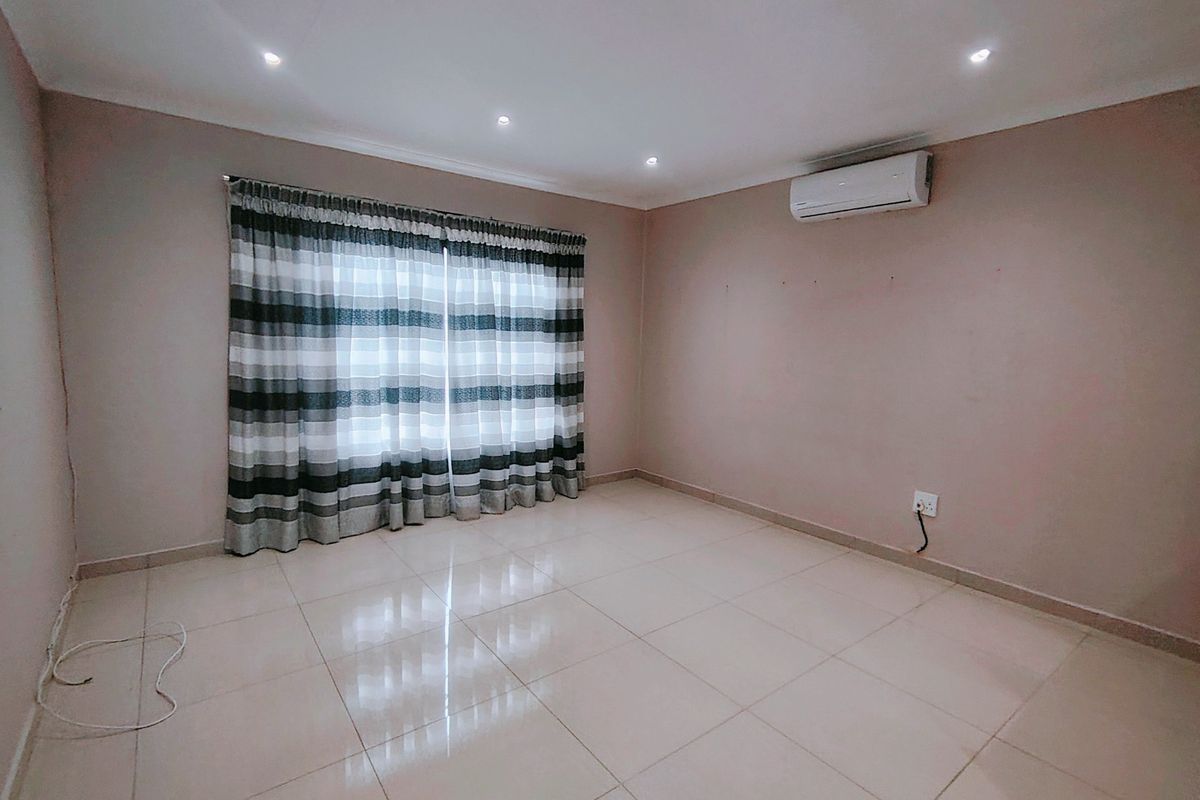A spacious, empty bedroom featuring neutral tiled flooring, recessed downlighting, and a wall-mounted split-system air conditioning unit.