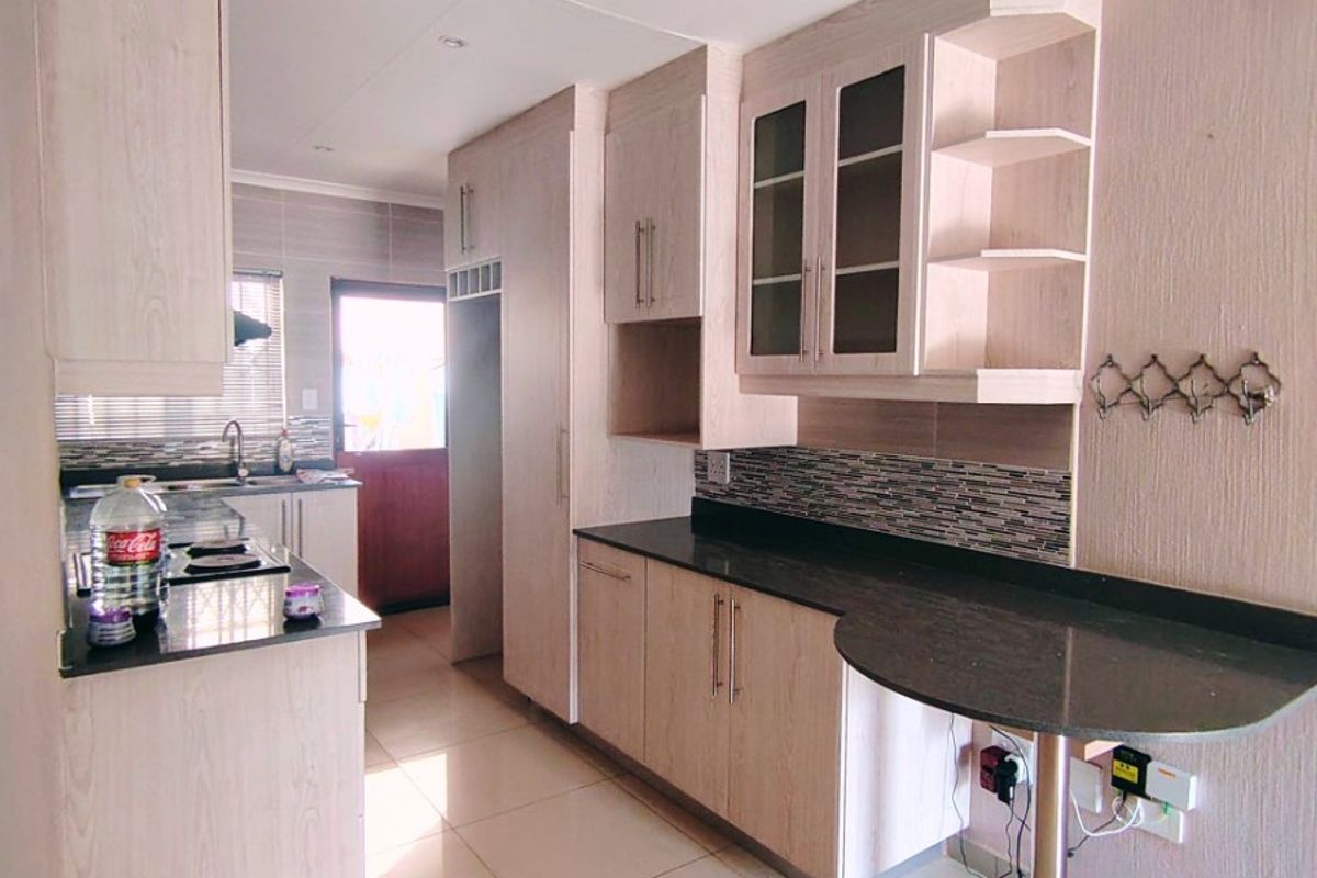 Modern kitchen featuring light wood-finish cabinetry, dark granite countertops, mosaic backsplash, and a convenient integrated breakfast bar with ceramic tiled flooring.