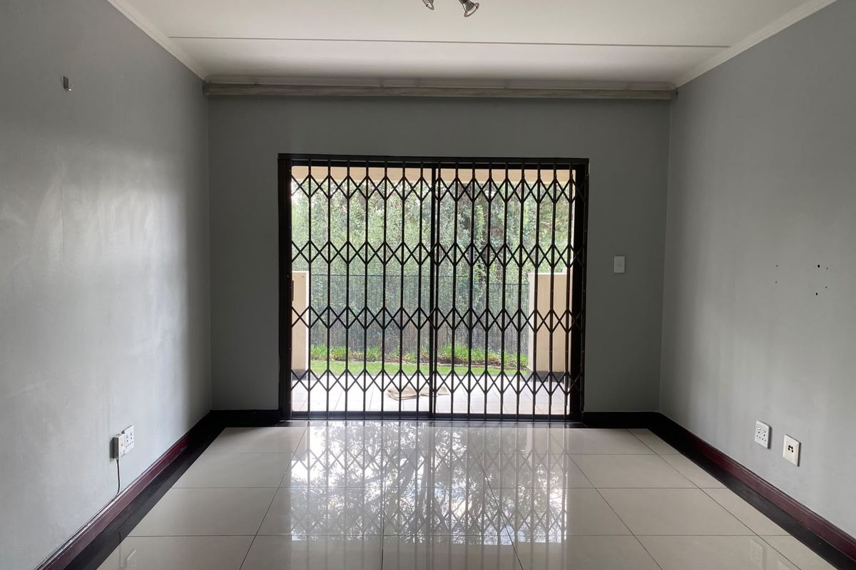 An empty living room featuring tiled flooring, neutral grey walls, and a sliding glass door with a security gate leading to an outdoor area.