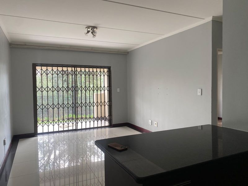 Open-plan living area featuring polished tile flooring, a granite breakfast bar, and a sliding glass door with a security gate leading to the exterior.