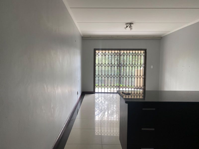 An empty open-plan living area featuring tiled flooring, a kitchen island, and a sliding door with a security gate leading to the exterior.