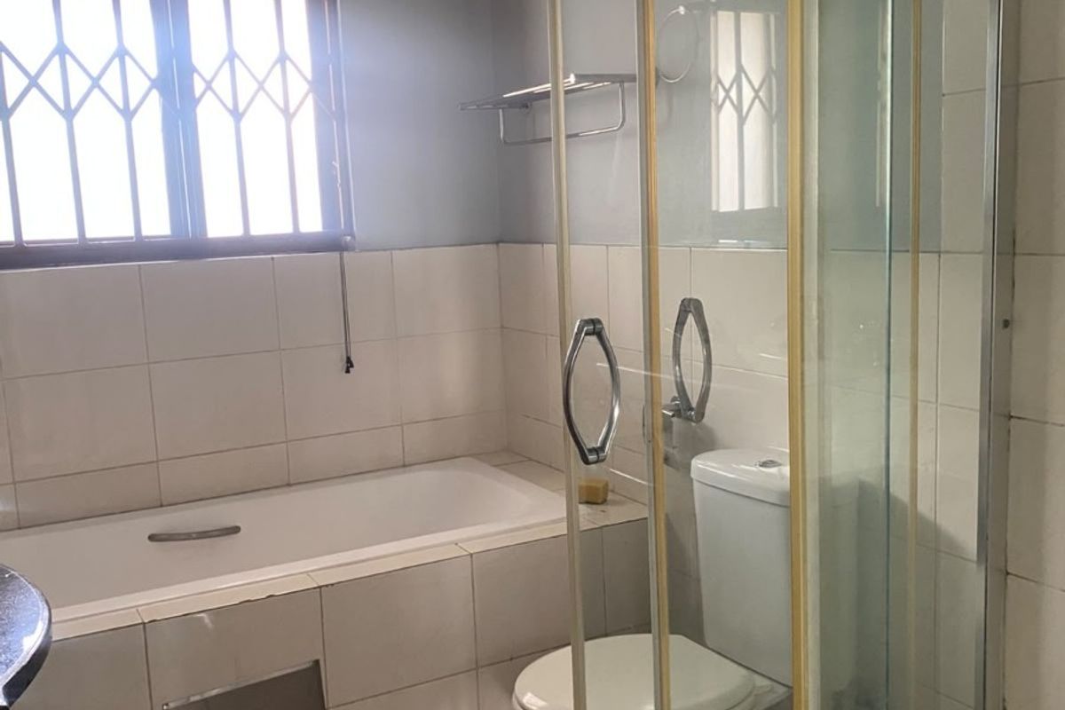 A functional bathroom featuring a built-in bathtub, a separate glass-enclosed shower, and tiled finishes throughout, offering a clean and practical layout.