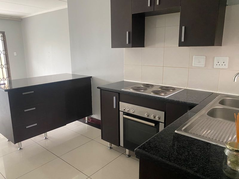 Modern kitchen featuring dark wood cabinetry, granite countertops, built-in oven, electric hob, and a stainless steel double sink with tiled flooring.