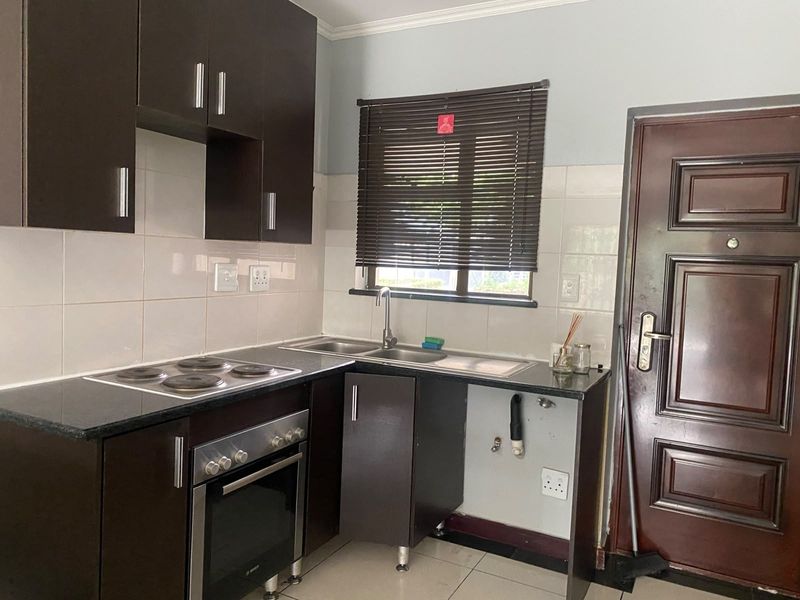 Compact kitchen featuring dark wood cabinetry, granite countertops, built-in oven and hob, tiled backsplash, and dedicated plumbing space for an under-counter appliance.