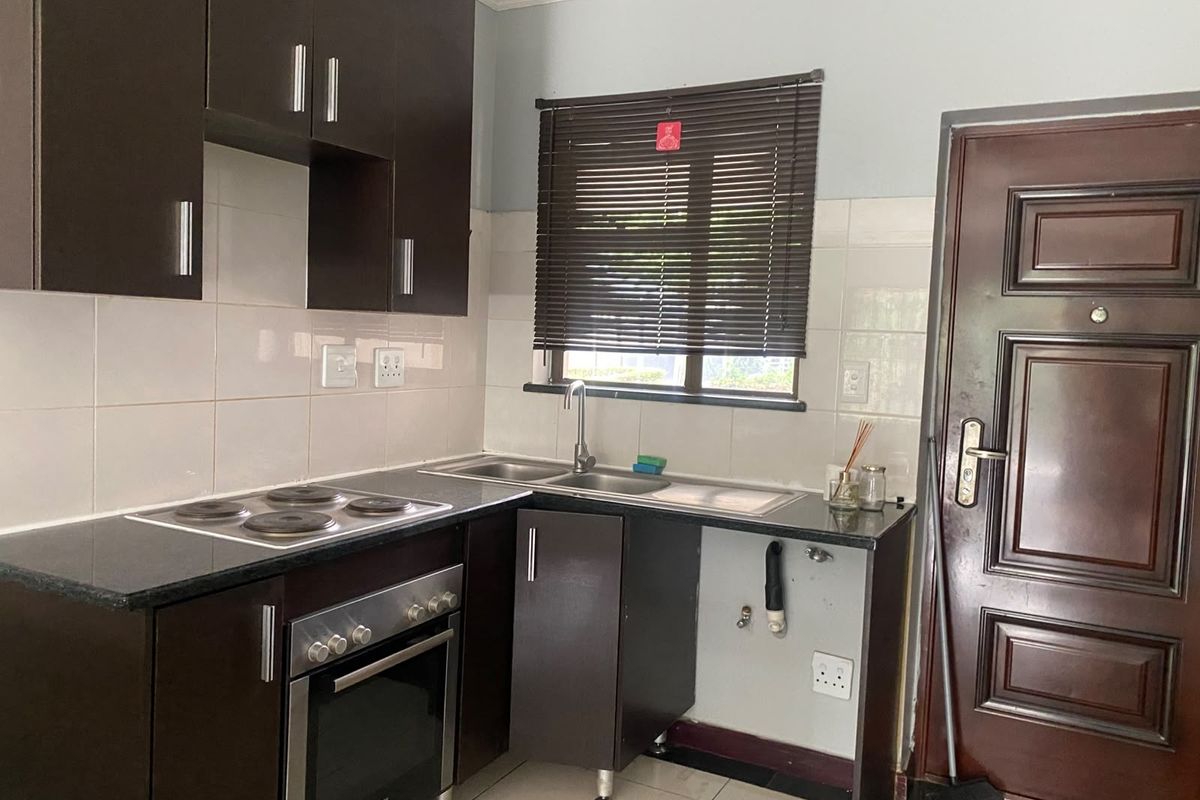 Compact kitchen featuring dark wood cabinetry, granite countertops, built-in oven and hob, tiled backsplash, and dedicated plumbing space for an under-counter appliance.