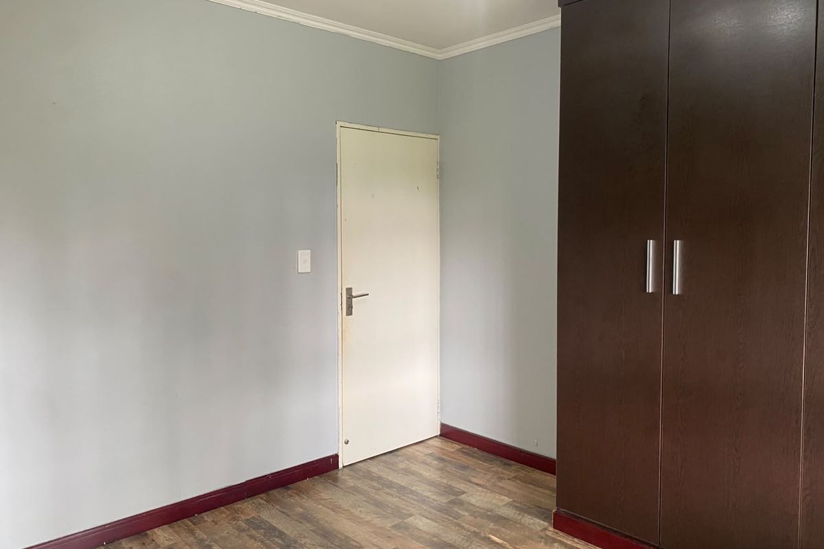 A clean, empty bedroom featuring laminate flooring, coving, and a large built-in dark wood wardrobe.