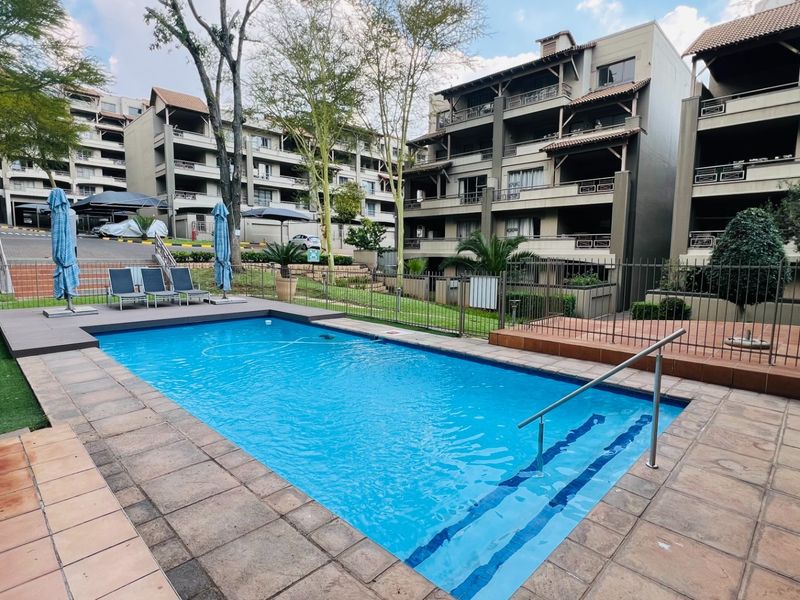 A well-maintained communal swimming pool area featuring tiled surrounds, metal safety fencing, and integrated steps within an apartment complex setting.
