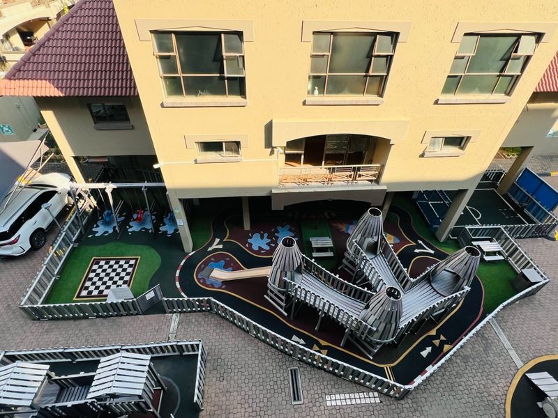 Aerial view of an apartment complex featuring a communal playground area, paved parking, and covered carports.