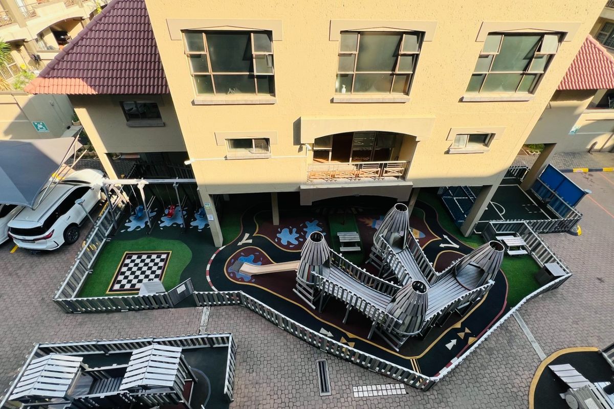 Aerial view of an apartment complex featuring a communal playground area, paved parking, and covered carports.