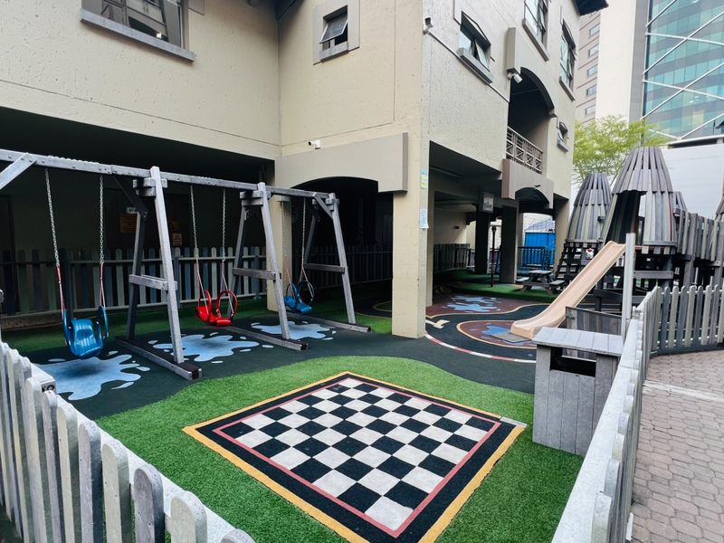 A communal outdoor playground area featuring synthetic grass, a built-in chess board, and various play structures within an apartment complex.