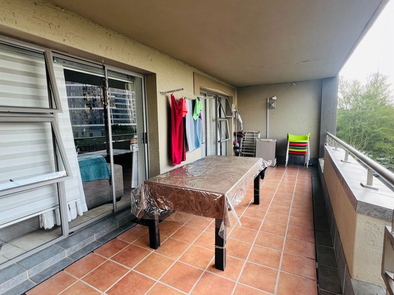 A spacious covered balcony featuring tiled flooring, metal balustrades, and large sliding glass doors providing access to the interior living area.