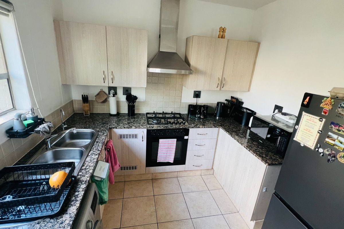 A functional kitchen featuring granite countertops, a gas hob with extractor fan, built-in oven, double sink, and light-toned laminate cabinetry.