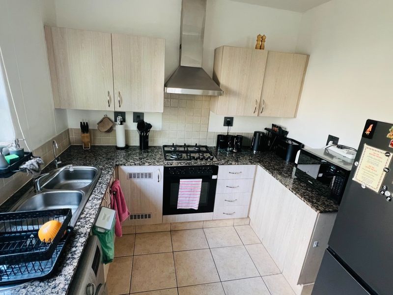 A functional kitchen featuring granite countertops, a gas hob with extractor fan, built-in oven, double sink, and light-toned laminate cabinetry.