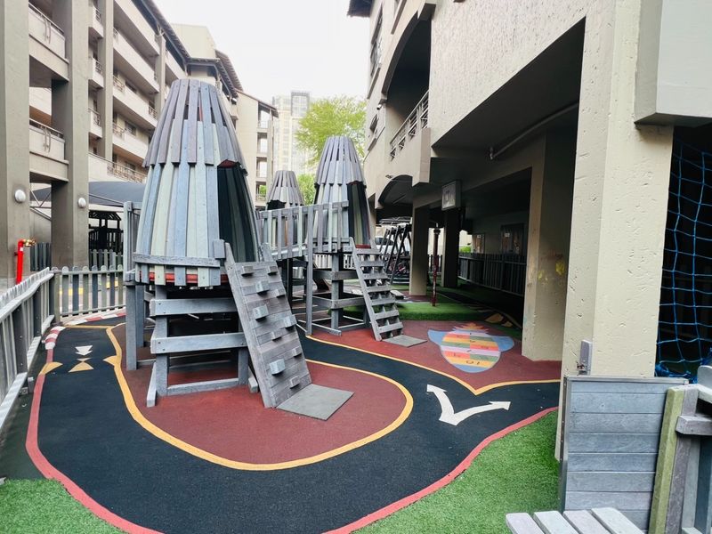 A communal outdoor playground area located within the apartment complex, featuring fixed play structures and safety flooring.