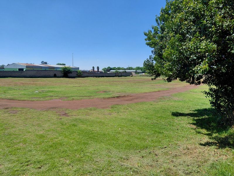 A wide, open vacant commercial land plot featuring a grass lawn and a perimeter boundary wall.