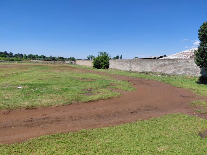 A view of a vacant commercial land plot featuring a dirt access path and a concrete block boundary wall.