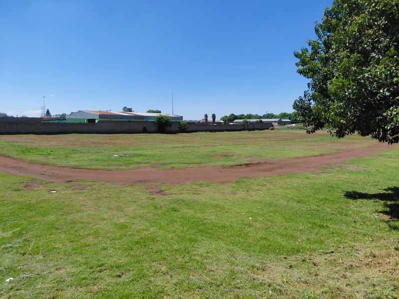 A wide view of a vacant commercial land plot featuring a grass lawn and a perimeter boundary wall.