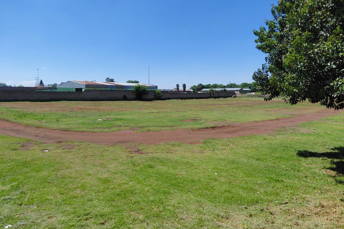 A wide view of a vacant commercial land plot featuring a grass lawn and a perimeter boundary wall.
