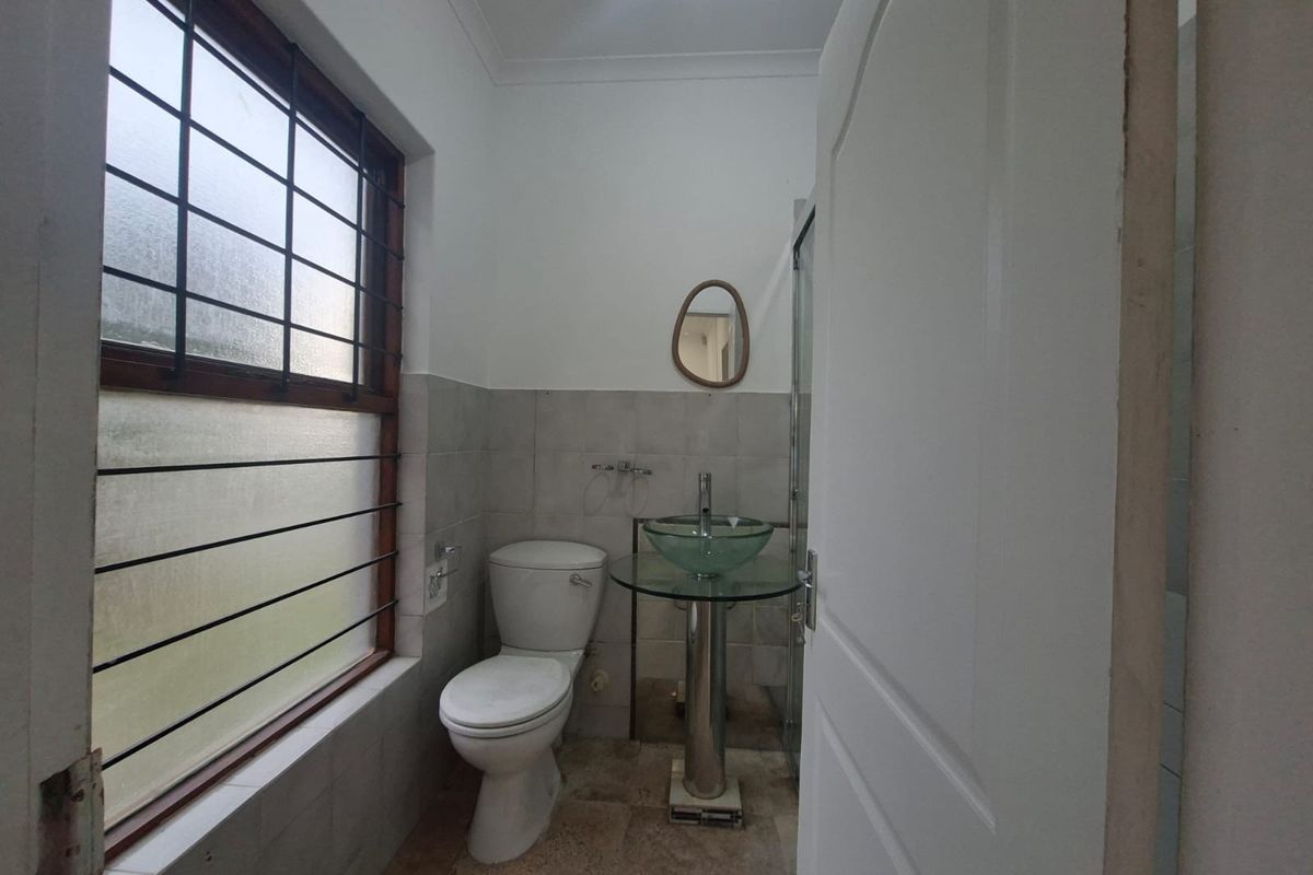 A compact bathroom featuring a pedestal basin, toilet, and shower enclosure with tiled finishes and security bars on the window.