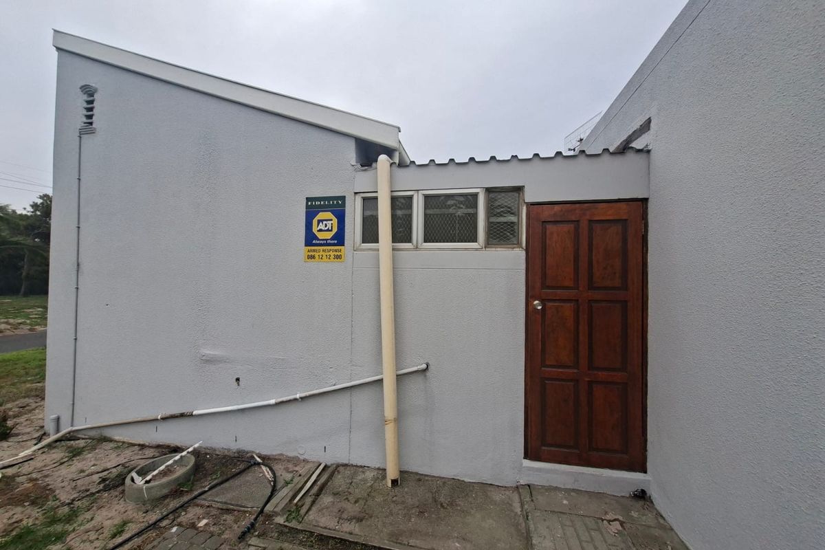 Rear exterior view of the townhouse showing a timber door, security window, and visible maintenance issues on the wall and drainage system.
