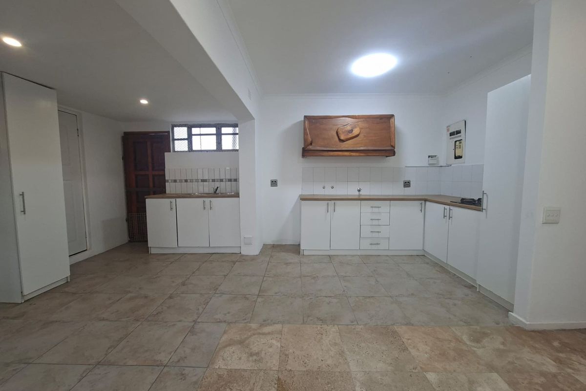 Spacious kitchen featuring white built-in cabinetry, laminate countertops, tiled flooring, and a dedicated cooking area with an extractor hood.