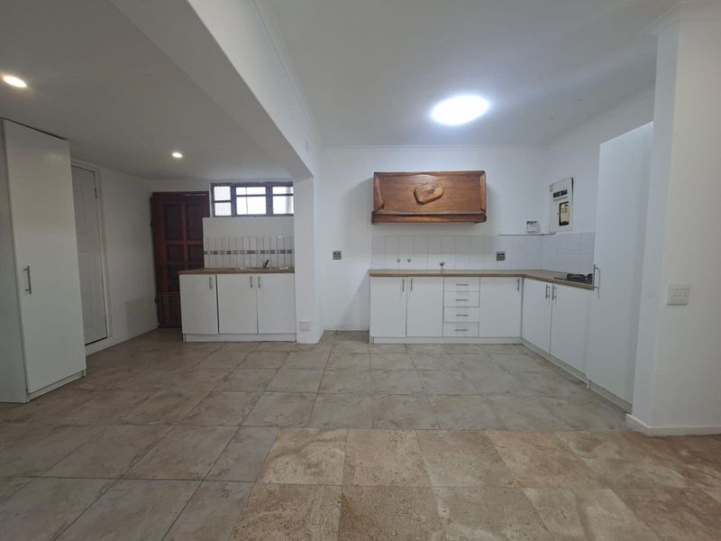 Spacious kitchen featuring white built-in cabinetry, laminate countertops, tiled flooring, and a dedicated cooking area with an extractor hood.