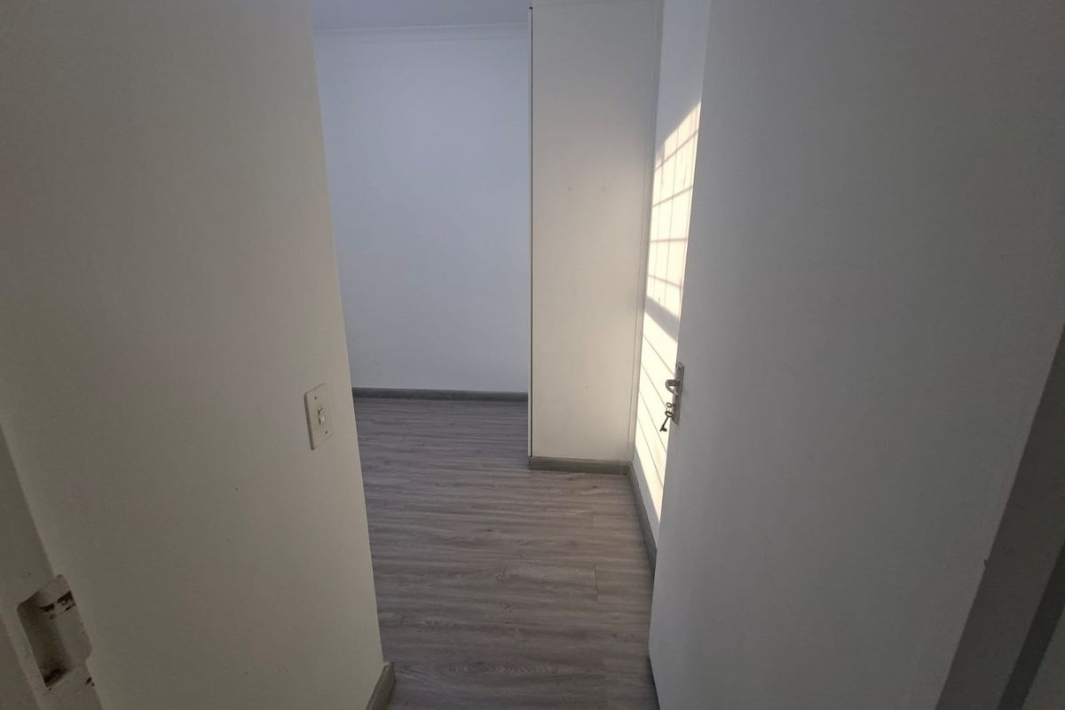 An empty bedroom featuring modern grey laminate flooring, neutral walls, and a built-in cupboard with natural light streaming through the window.
