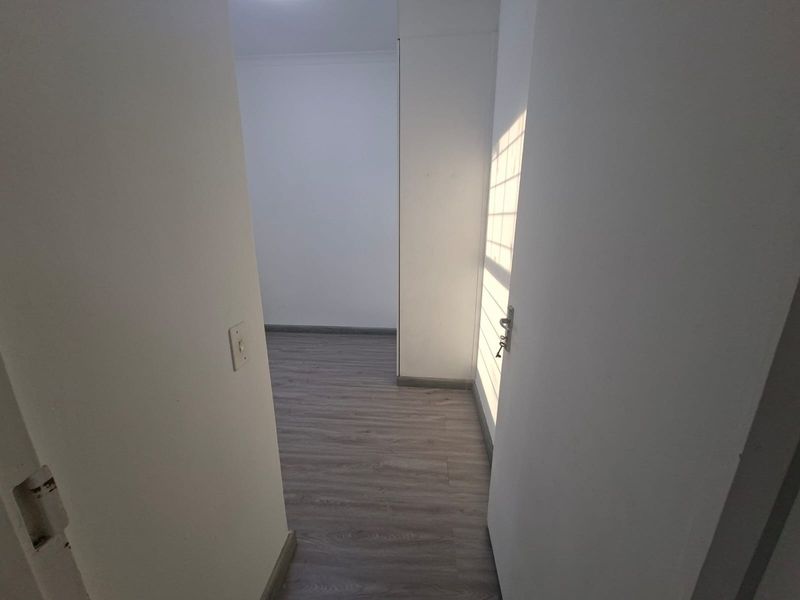 An empty bedroom featuring modern grey laminate flooring, neutral walls, and a built-in cupboard with natural light streaming through the window.