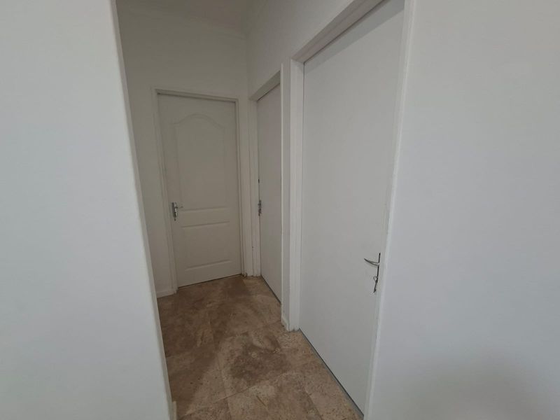 A clean and simple hallway featuring neutral tiled flooring and multiple internal doors providing access to adjacent rooms.