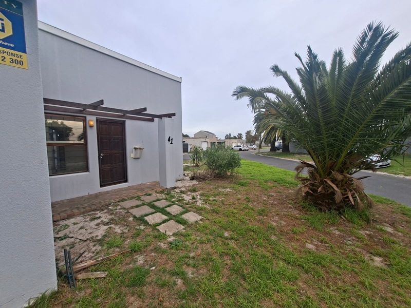 Front exterior view of the townhouse featuring a timber pergola, paved entrance path, and established garden area.