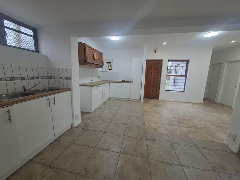 Open-plan kitchen and living area featuring tiled flooring, white cabinetry, and secure window bars, offering a functional blank canvas for renovation.