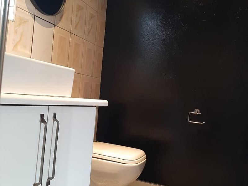 A modern bathroom featuring a white vanity cabinet, basin, toilet, and striking patterned floor tiles contrasted by a bold black feature wall.