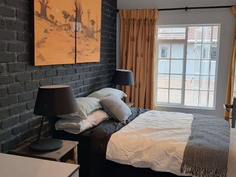 A well-maintained bedroom featuring a striking dark exposed brick feature wall, polished concrete floors, and a large casement window allowing natural light.