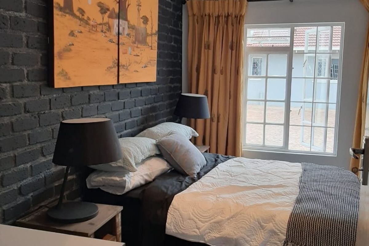 A well-maintained bedroom featuring a striking dark exposed brick feature wall, polished concrete floors, and a large casement window allowing natural light.