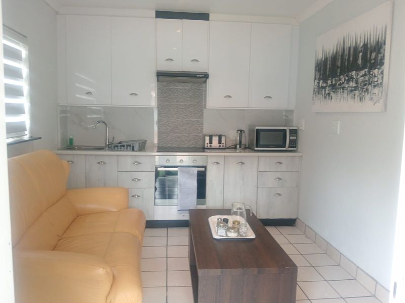 Compact open-plan kitchen and living area featuring modern white cabinetry, integrated appliances, tiled flooring, and a functional layout suitable for apartment living.