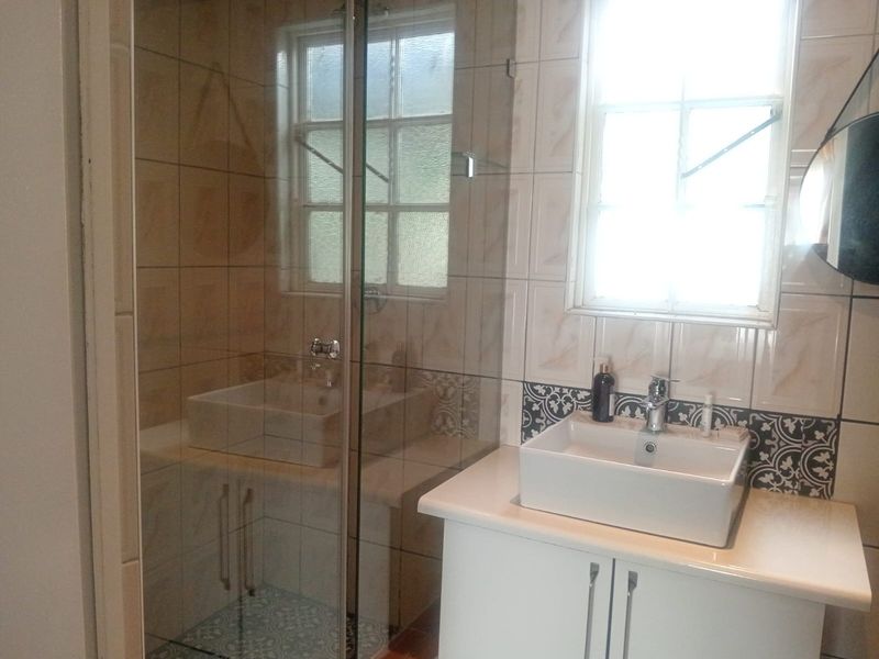 A modern bathroom featuring a glass-enclosed shower, a contemporary vessel sink with vanity storage, and decorative patterned tiling.