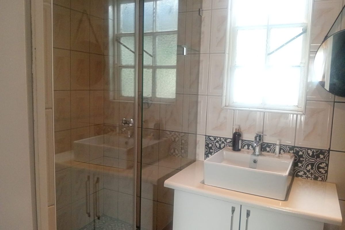 A modern bathroom featuring a glass-enclosed shower, a contemporary vessel sink with vanity storage, and decorative patterned tiling.