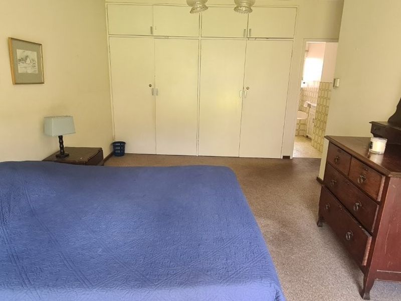 A bedroom featuring built-in cupboards and direct access to an en-suite bathroom, offering a functional layout with potential for modernization.