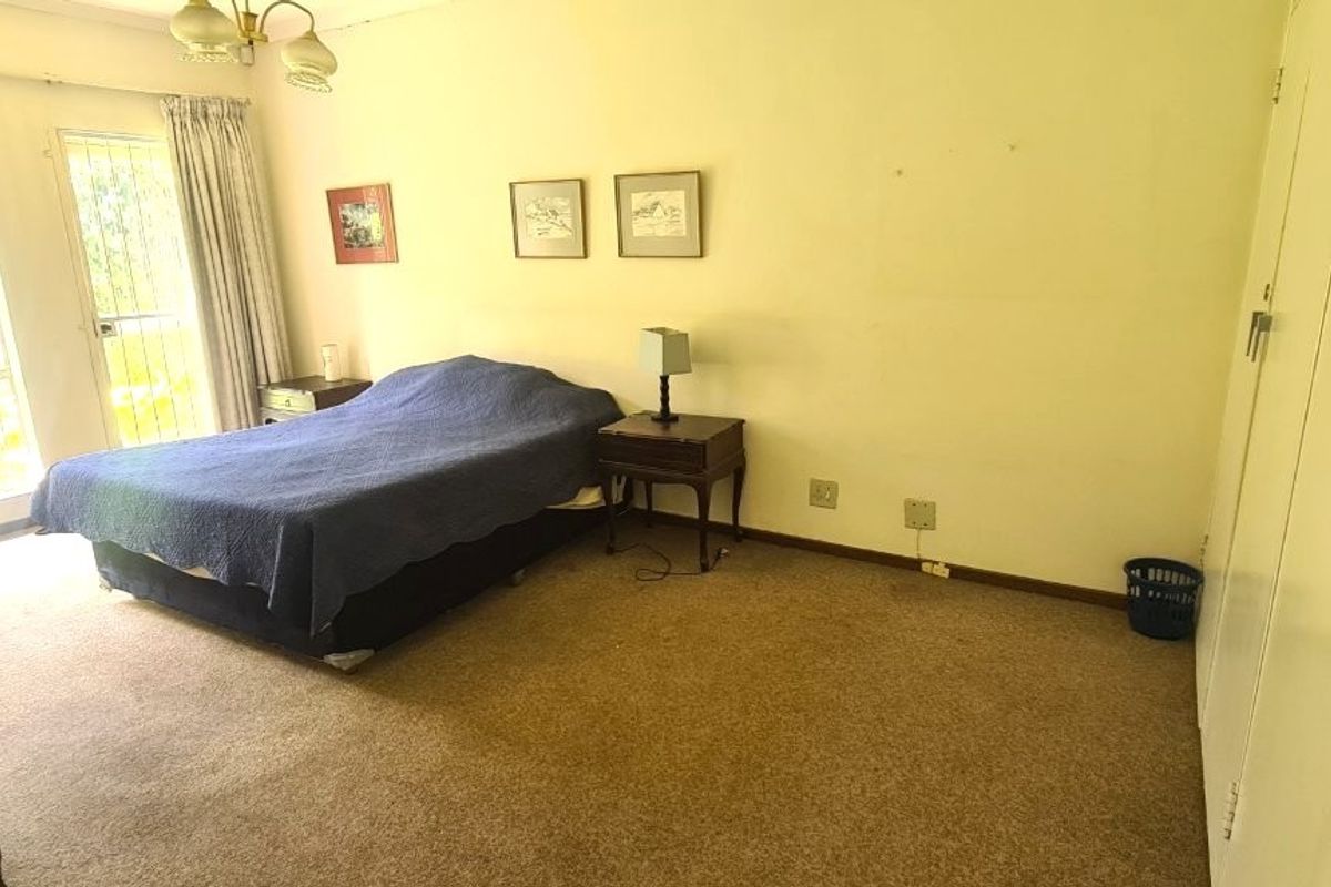 Spacious bedroom featuring built-in cupboards, carpeted flooring, and large windows with security bars, offering a functional layout ready for cosmetic updates.