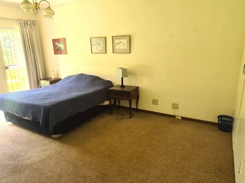 Spacious bedroom featuring built-in cupboards, carpeted flooring, and large windows with security bars, offering a functional layout ready for cosmetic updates.