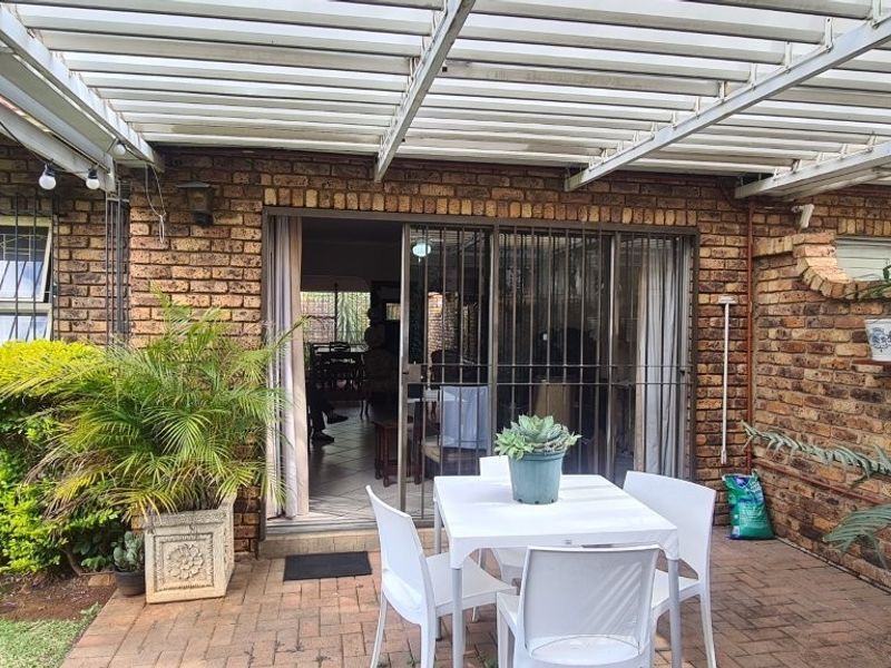 A covered outdoor patio area featuring brick walls, paved flooring, and a pergola, providing a functional space for outdoor dining and relaxation.