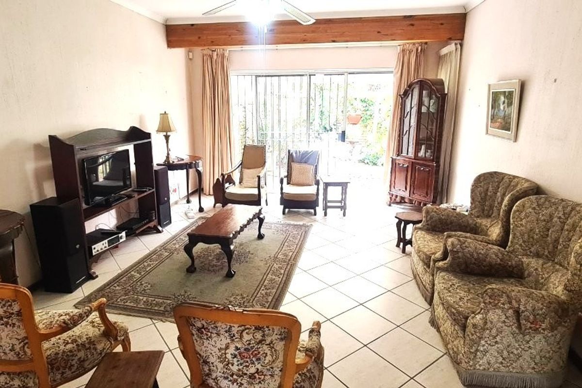 A spacious living room featuring tiled flooring, an exposed timber ceiling beam, and large sliding glass doors providing access to the outdoor area.