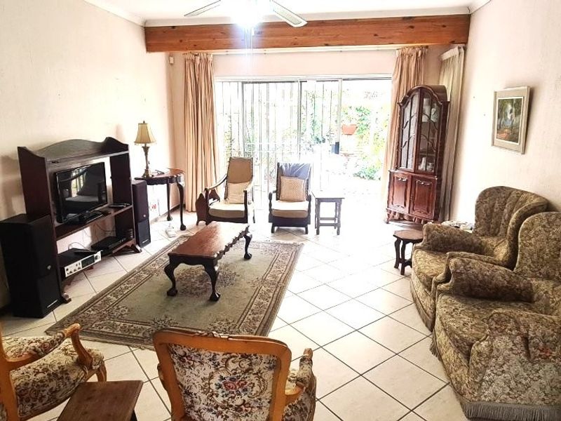 A spacious living room featuring tiled flooring, an exposed timber ceiling beam, and large sliding glass doors providing access to the outdoor area.